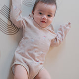 Baby in a light pink onesie lying on a white floor with a patterned rug.