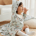 Child wearing a floral outfit with a blanket on head in a cozy indoor setting