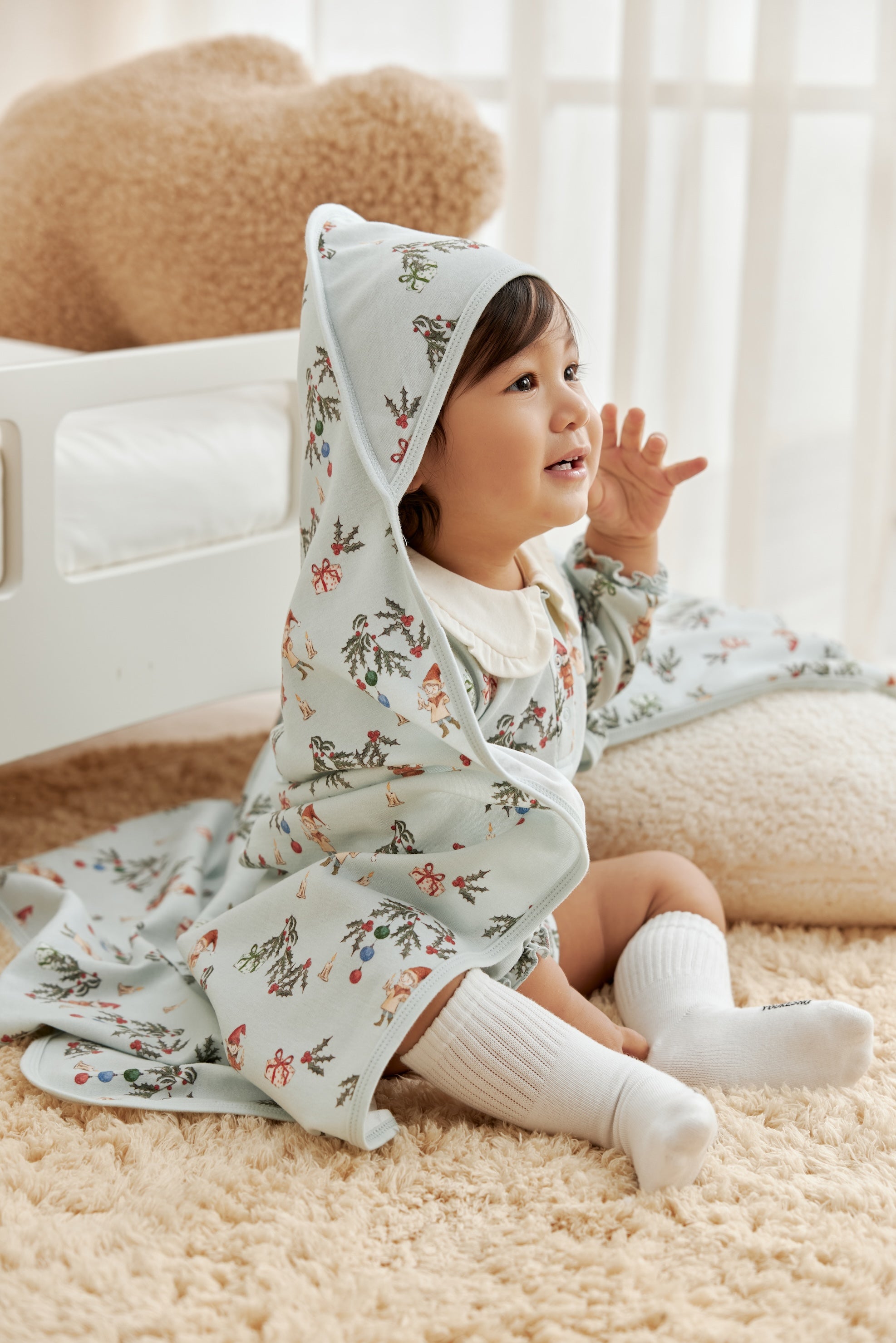 Child wearing a floral outfit with a blanket on head in a cozy indoor setting