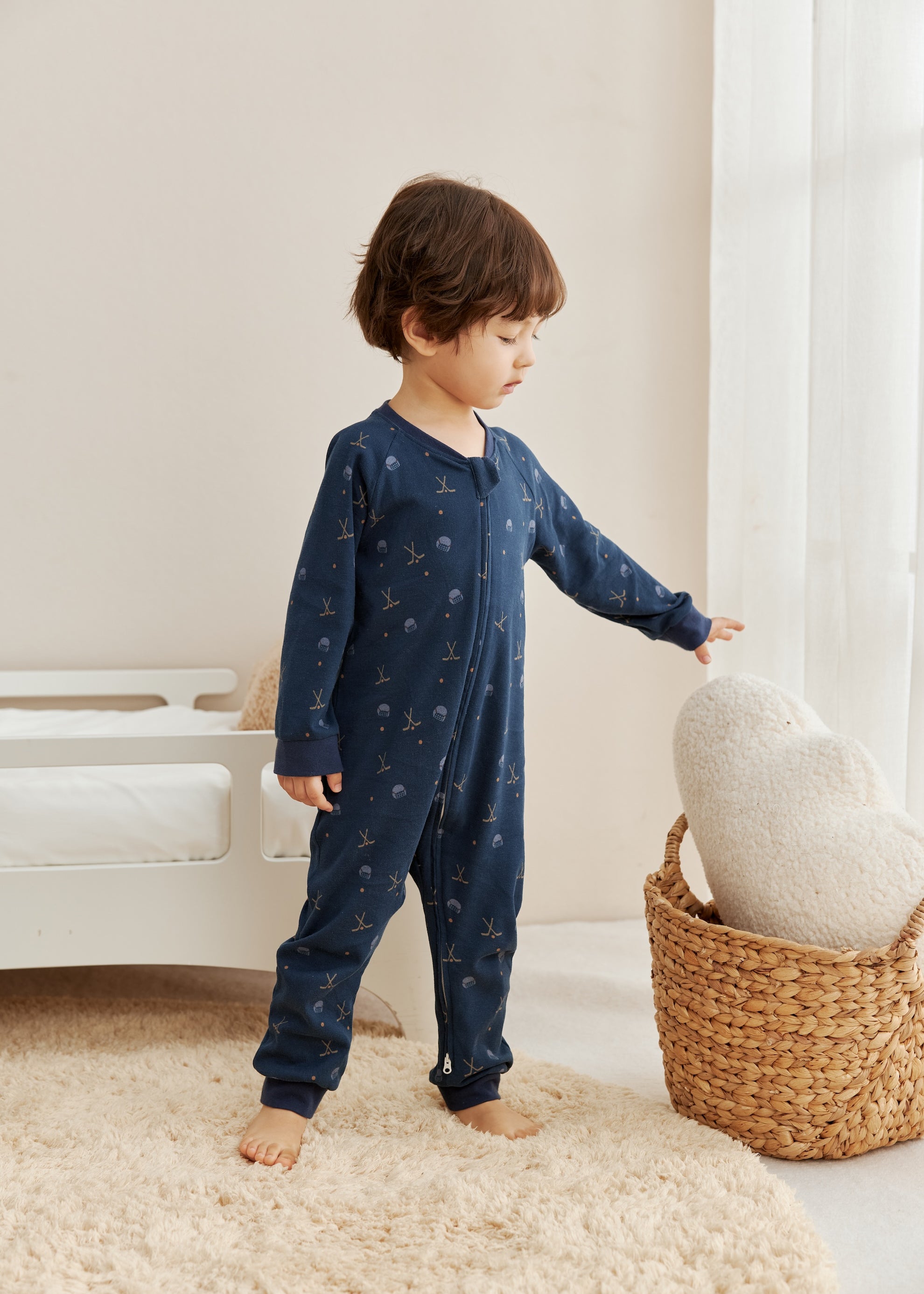 Child wearing a navy blue sleeper with star pattern, standing next to a woven basket on a light-colored rug.