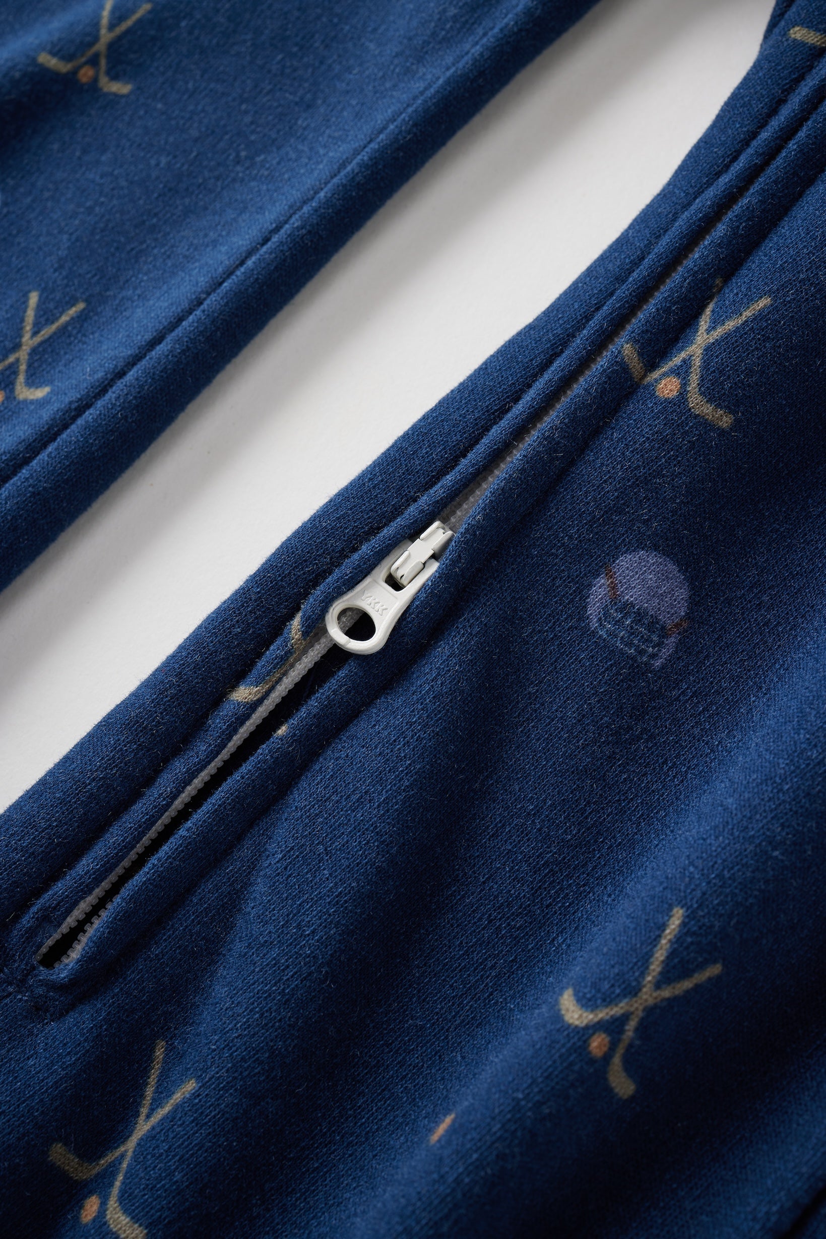 Close-up of a blue garment with a zipper and embroidered designs on a white background