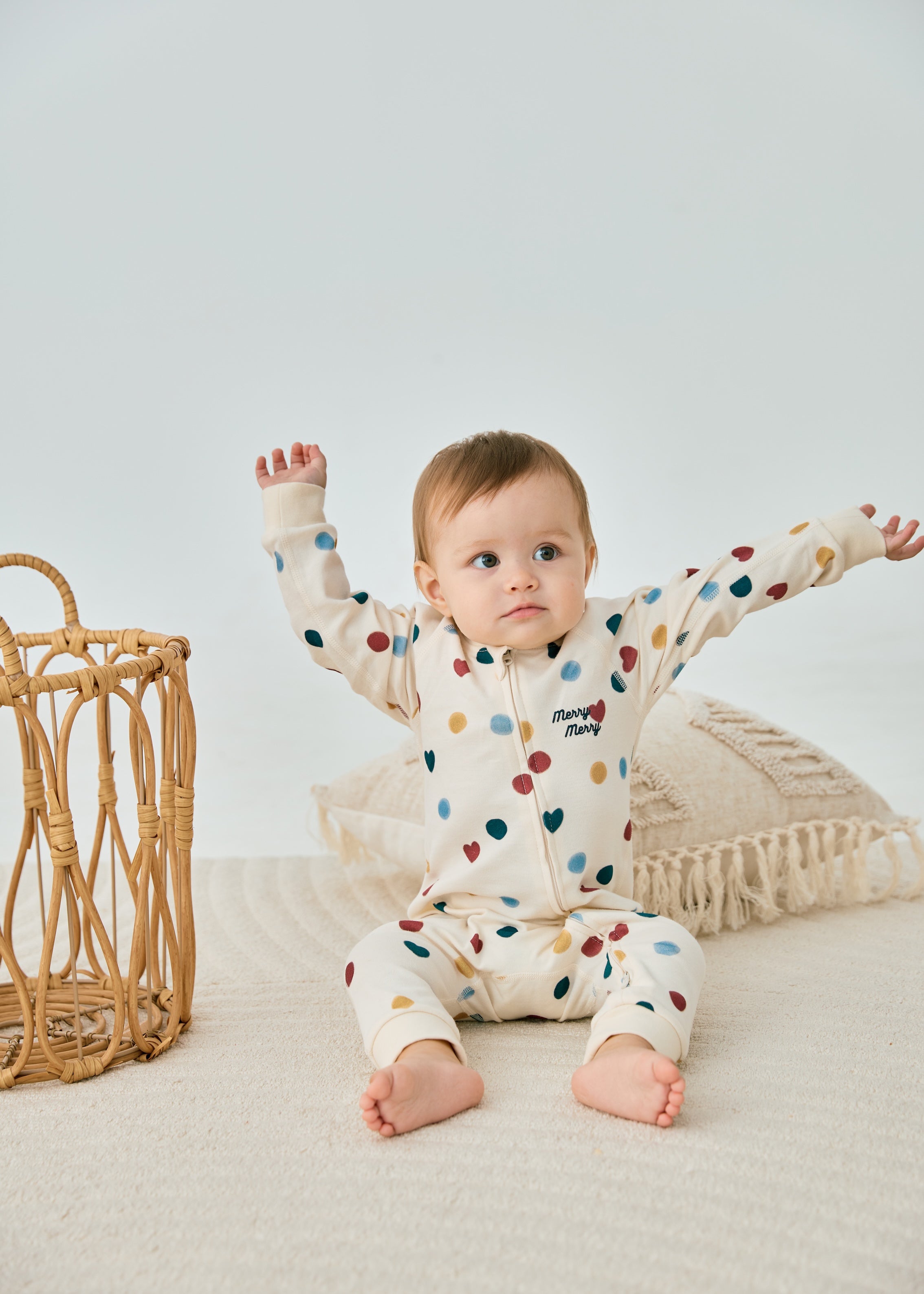 model sitting on the floor and wearing norsu organic baby organic cotton zip-up sleeper merry dots