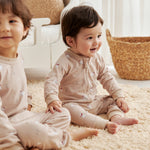 Two children sitting on a carpeted floor in a bright room with natural light.