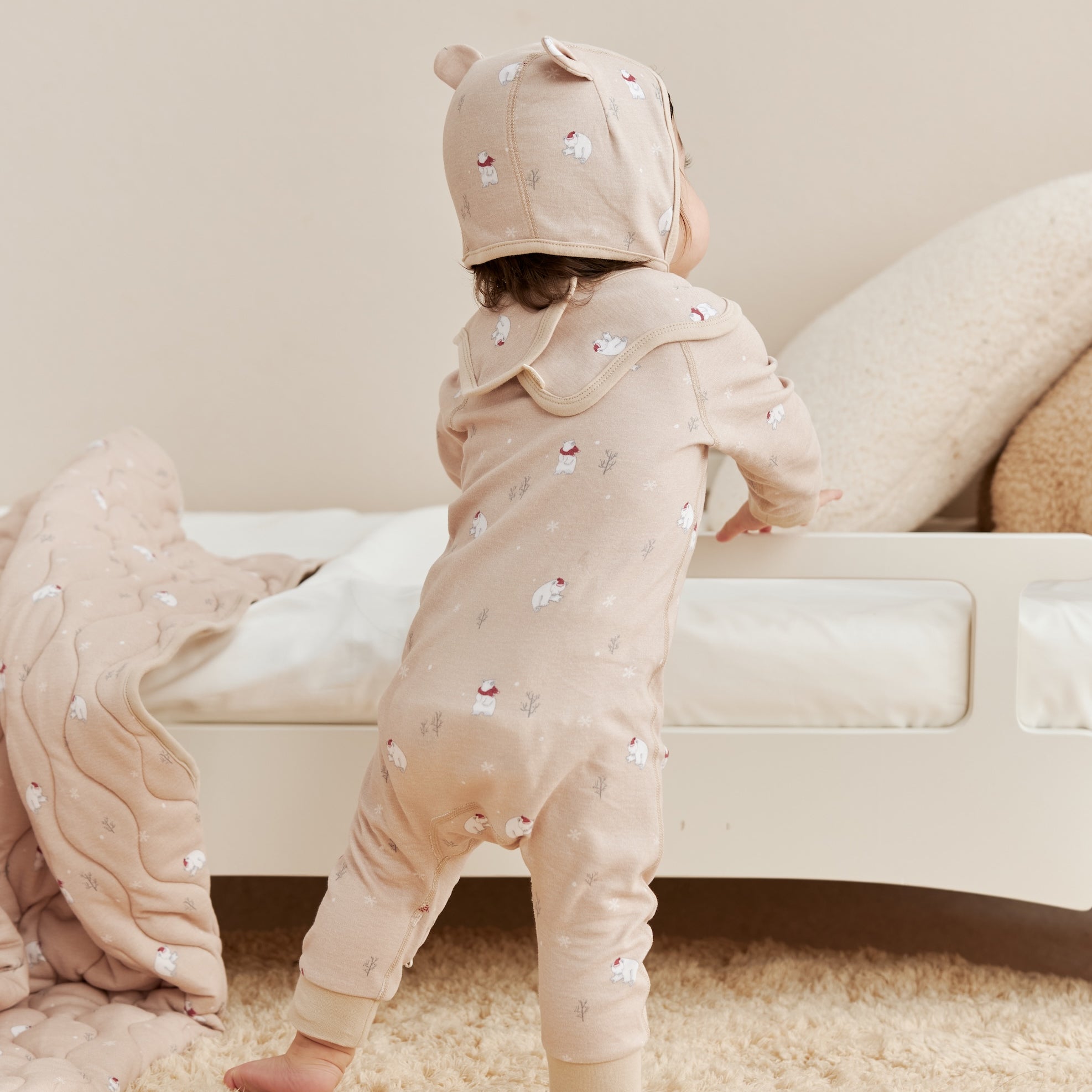 Two children in matching beige sleeper with polar bear patterns standing on a carpeted floor.