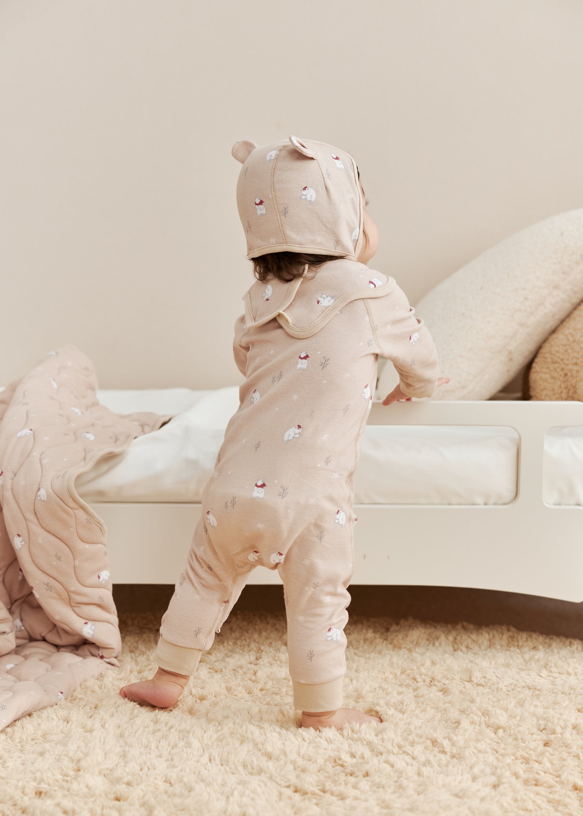 Two children in matching beige sleeper with polar bear patterns standing on a carpeted floor.
