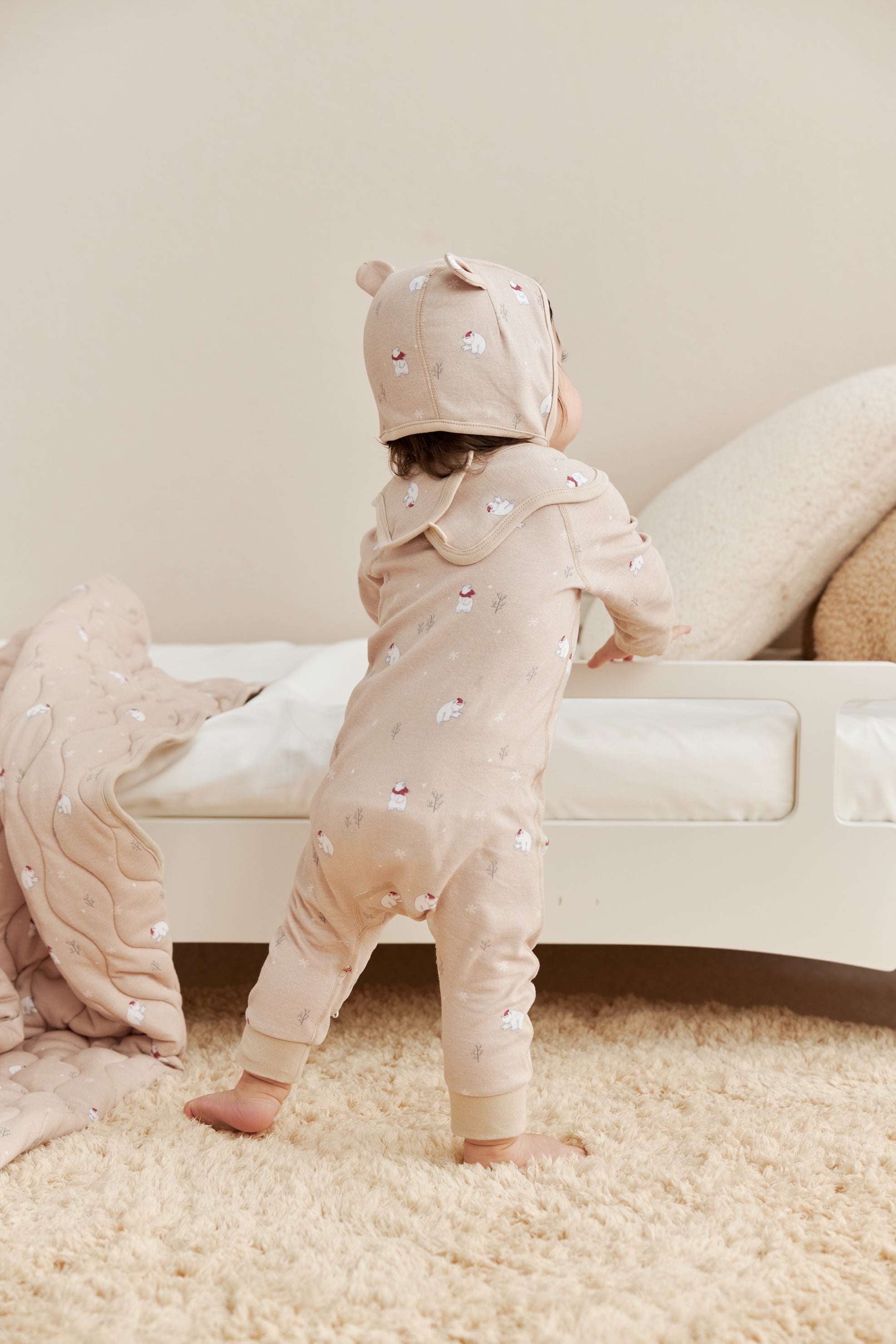 Two children in matching beige sleeper with polar bear patterns standing on a carpeted floor.