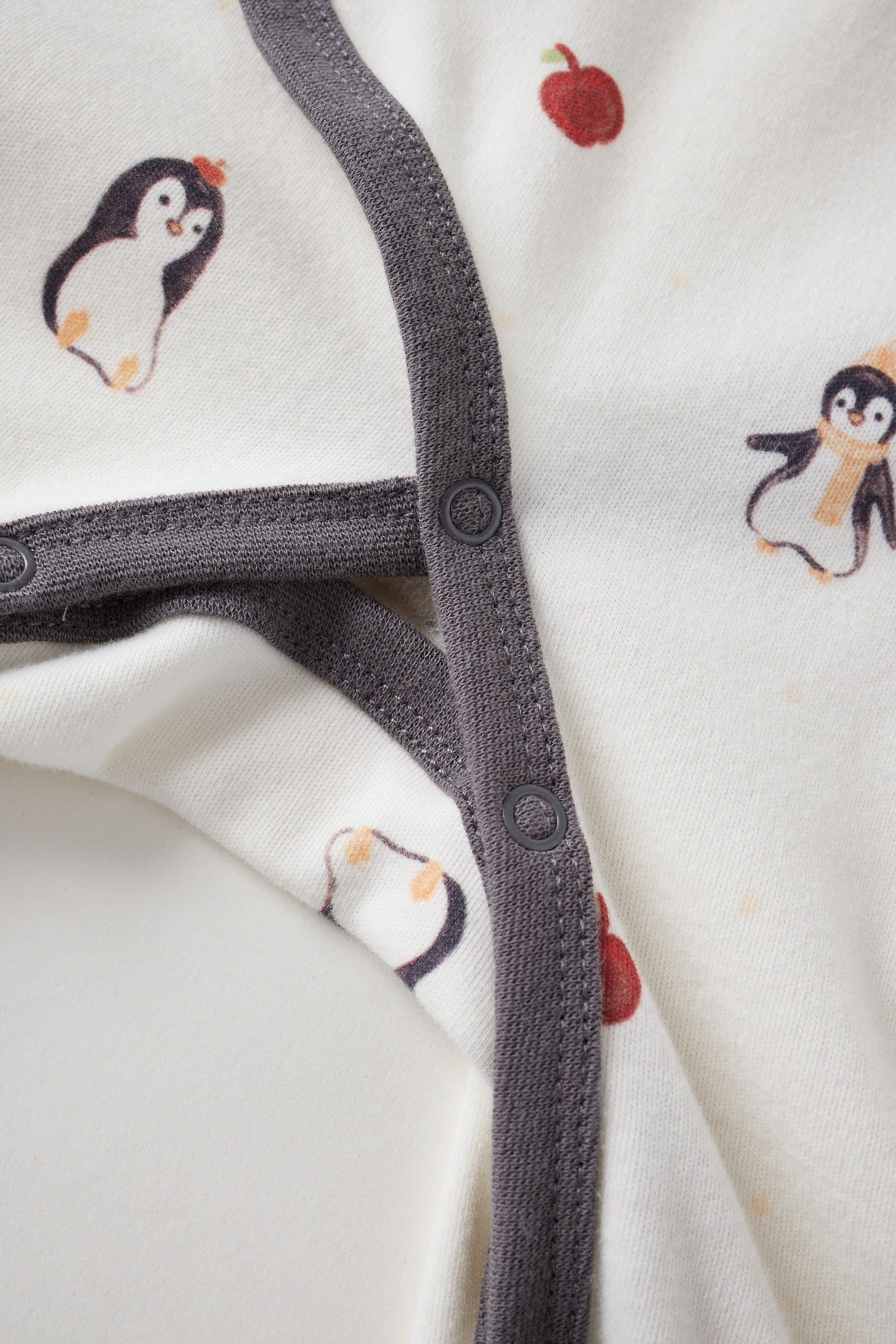 Close-up of a baby outfit with penguin and apple designs on a white background