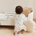 Child in a white kimono sleeper with animal prints standing on a beige carpet next to a white couch.