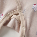 Close-up of a beige baby onesie with button details and small animal prints.