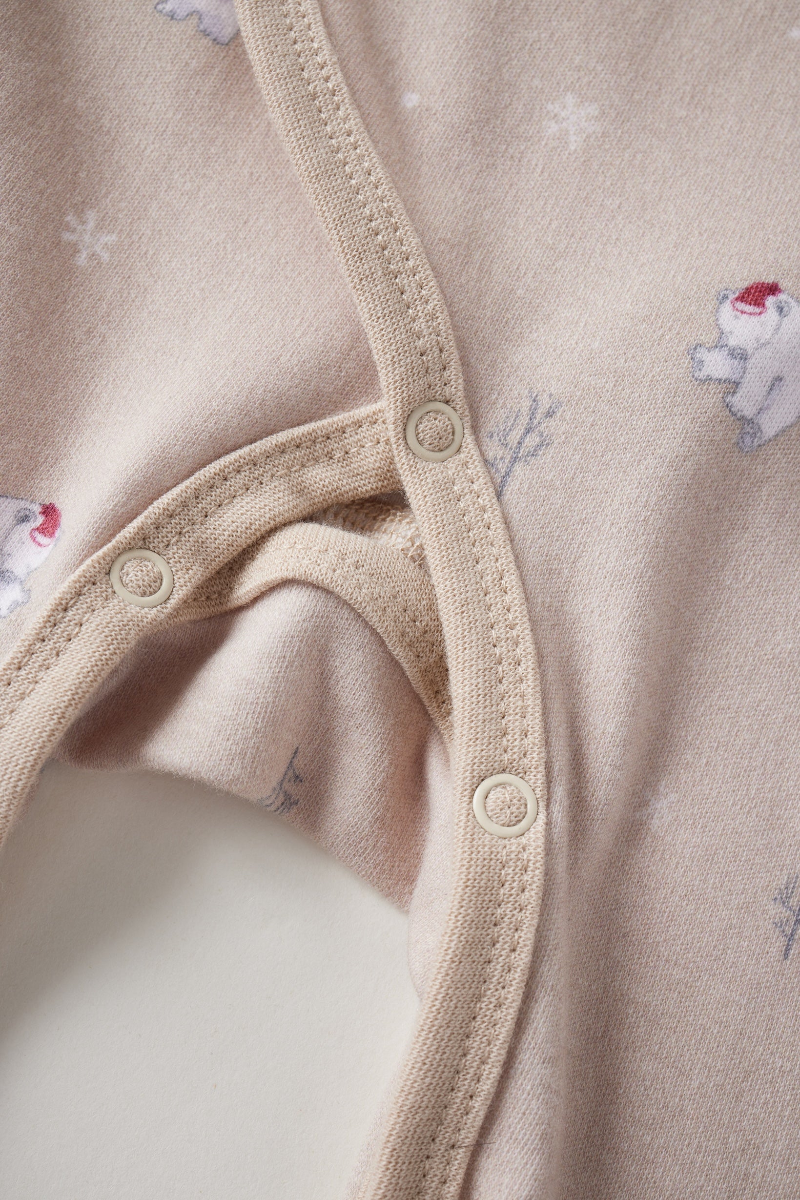 Close-up of a beige baby onesie with button details and small animal prints.