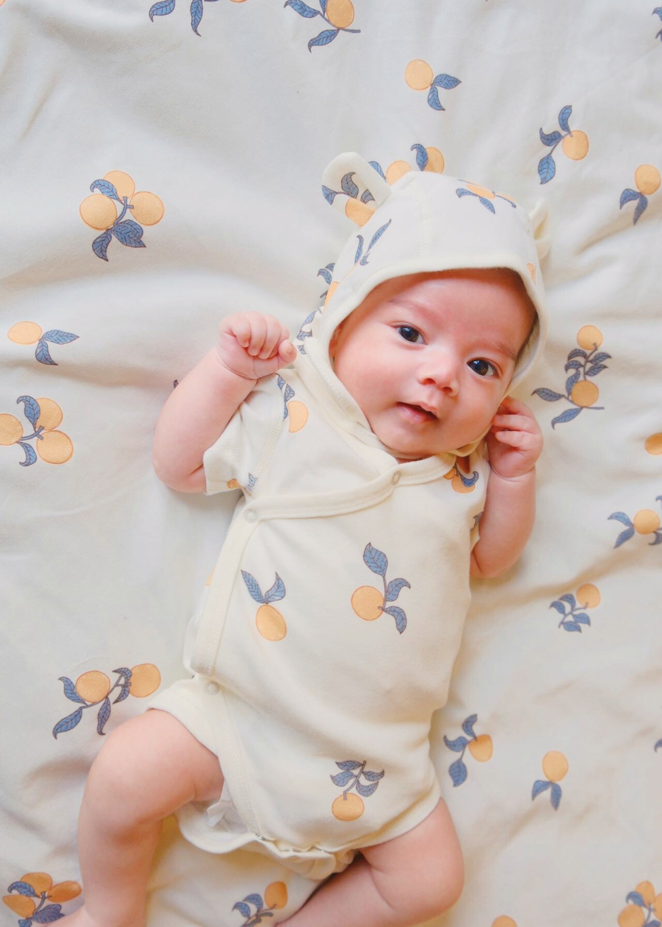 Sweet baby dressed in Baby Organic Kimono Short-sleeve Onesie-Clementine paired with trendy organic cotton bonnet hat for a comfy outfit