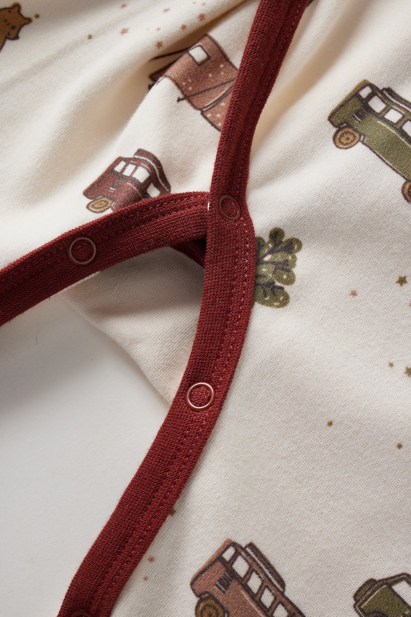 Close-up of a red strap on a garment with a pattern of brown cars on a beige background.