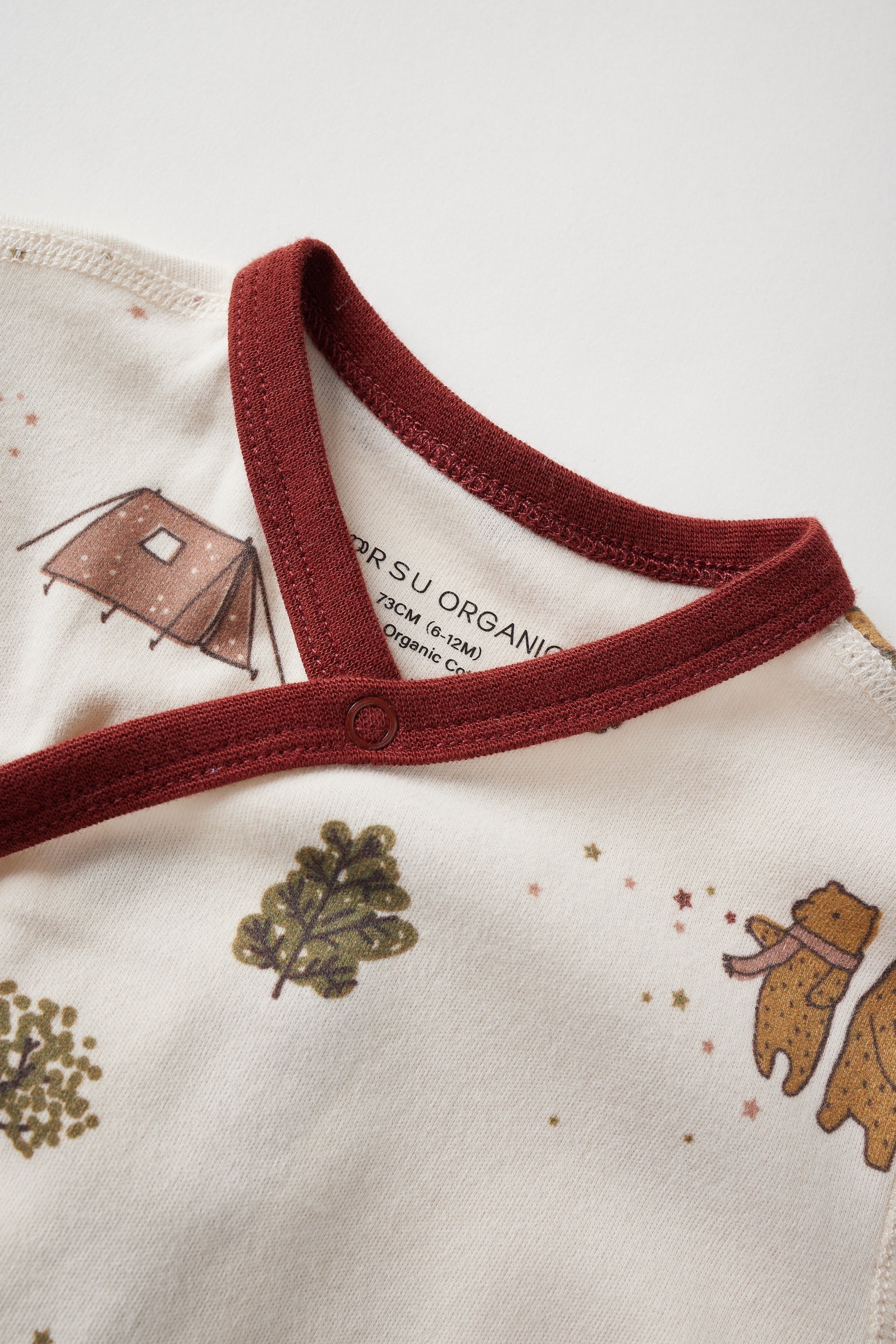 Close-up of a baby outfit with red collar and nature-themed design on a white background