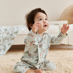 Baby in jolly pajamas sitting on a carpeted floor