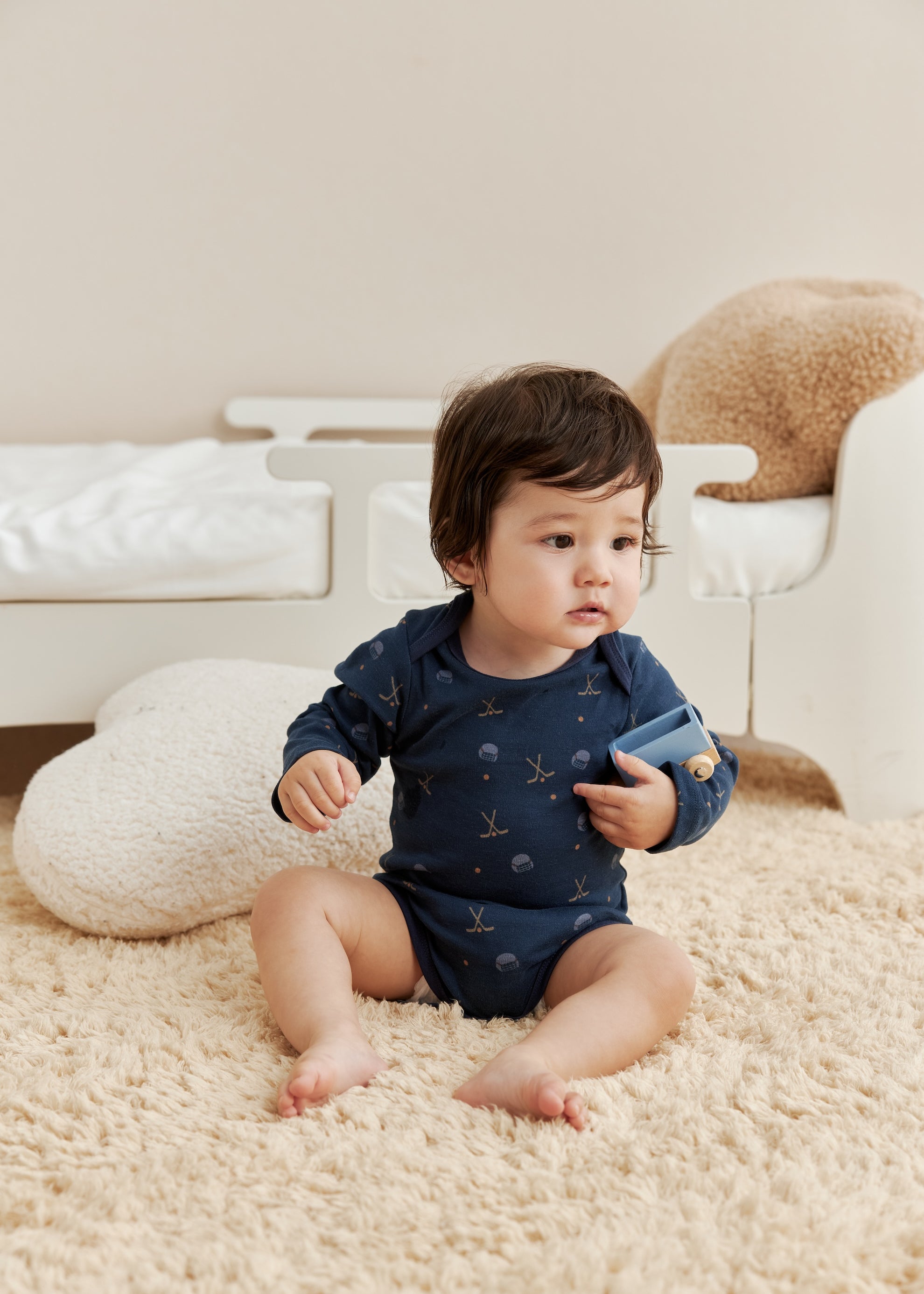 Baby in a blue onesie sitting on a beige carpet