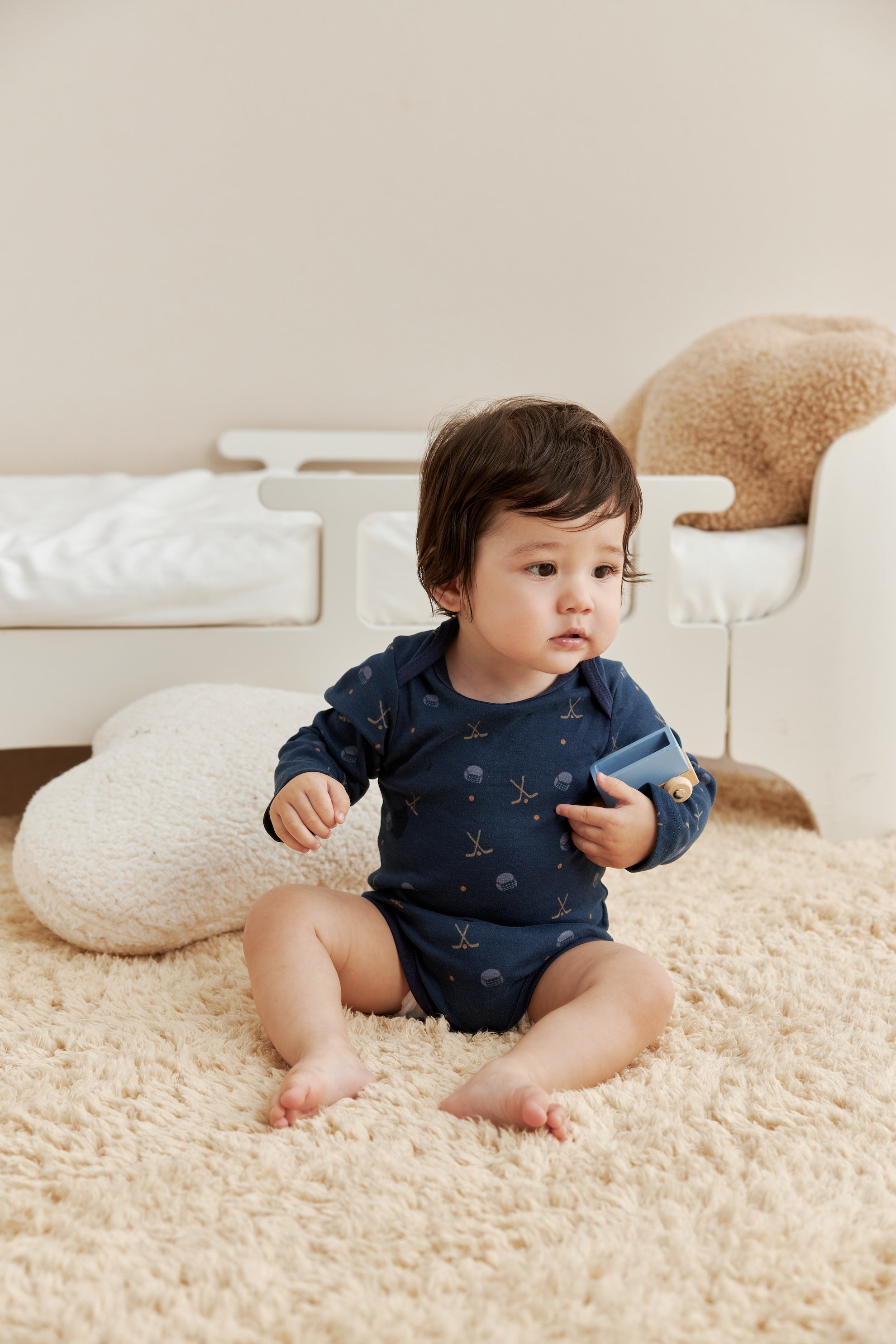 Baby in a blue onesie sitting on a beige carpet