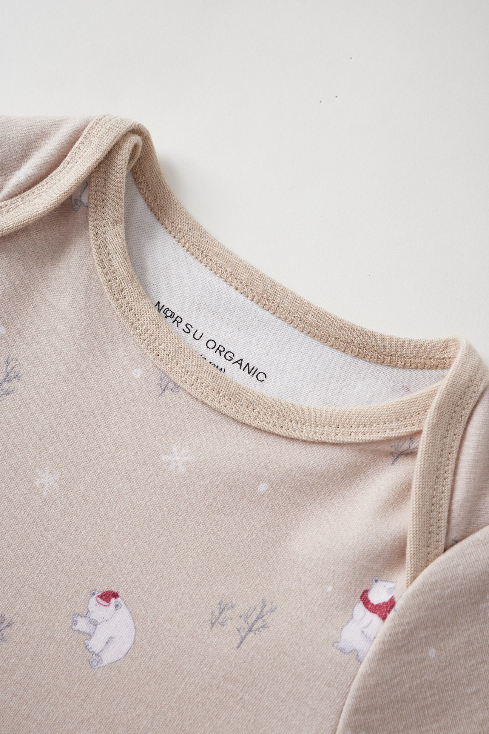 Close-up of a beige baby onesie with polar bear designs and 'Norsu Organic' label.
