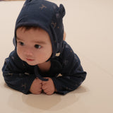 Baby wearing a dark blue onesie with hockey patterns on a light-colored surface.