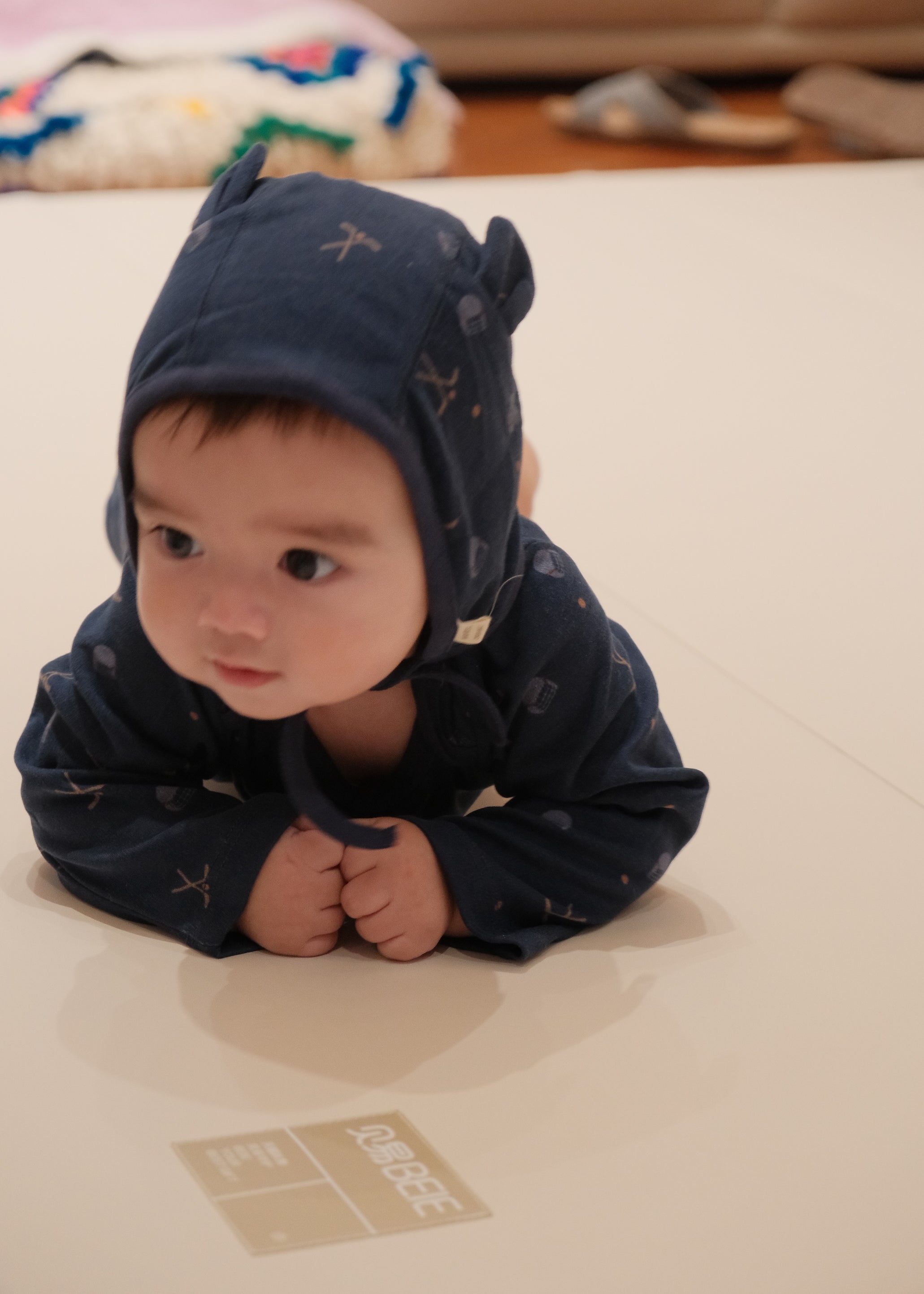 Baby wearing a dark blue onesie with hockey patterns on a light-colored surface.