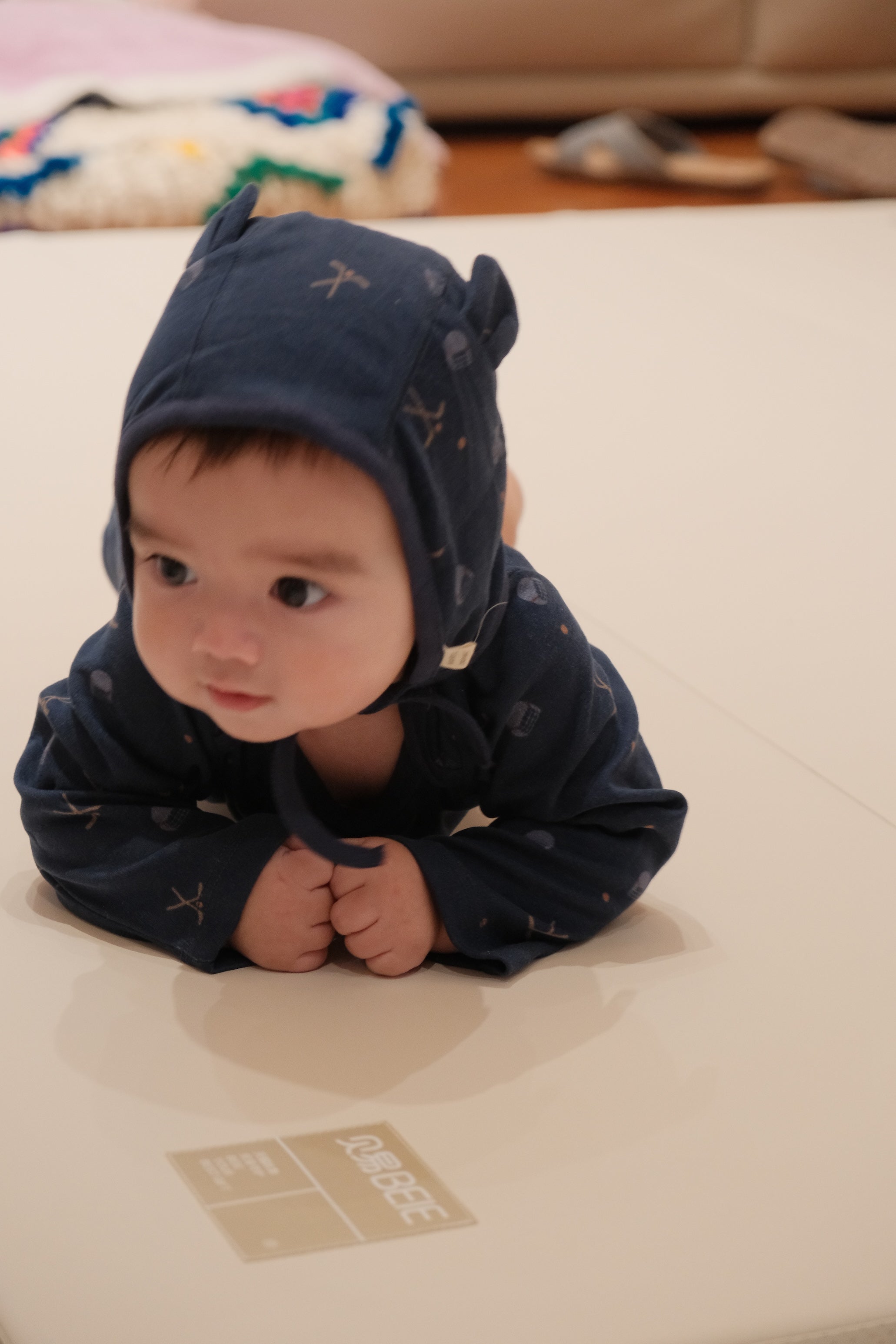 Baby wearing a dark blue onesie with hockey patterns on a light-colored surface.