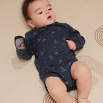 Baby wearing a navy blue onesie with patterns, lying on a beige surface.