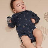 Baby wearing a navy blue onesie with patterns, lying on a beige surface.