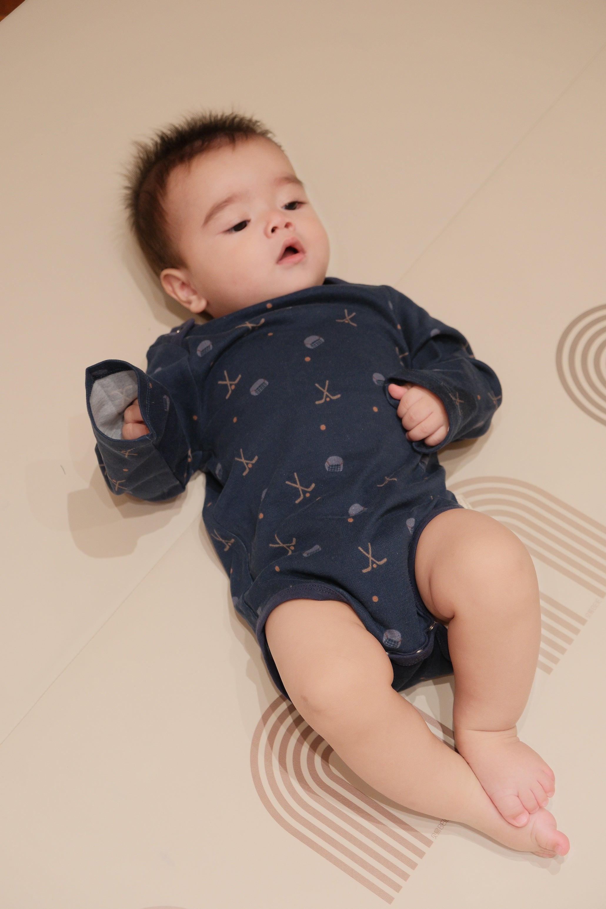 Baby wearing a navy blue onesie with patterns, lying on a beige surface.