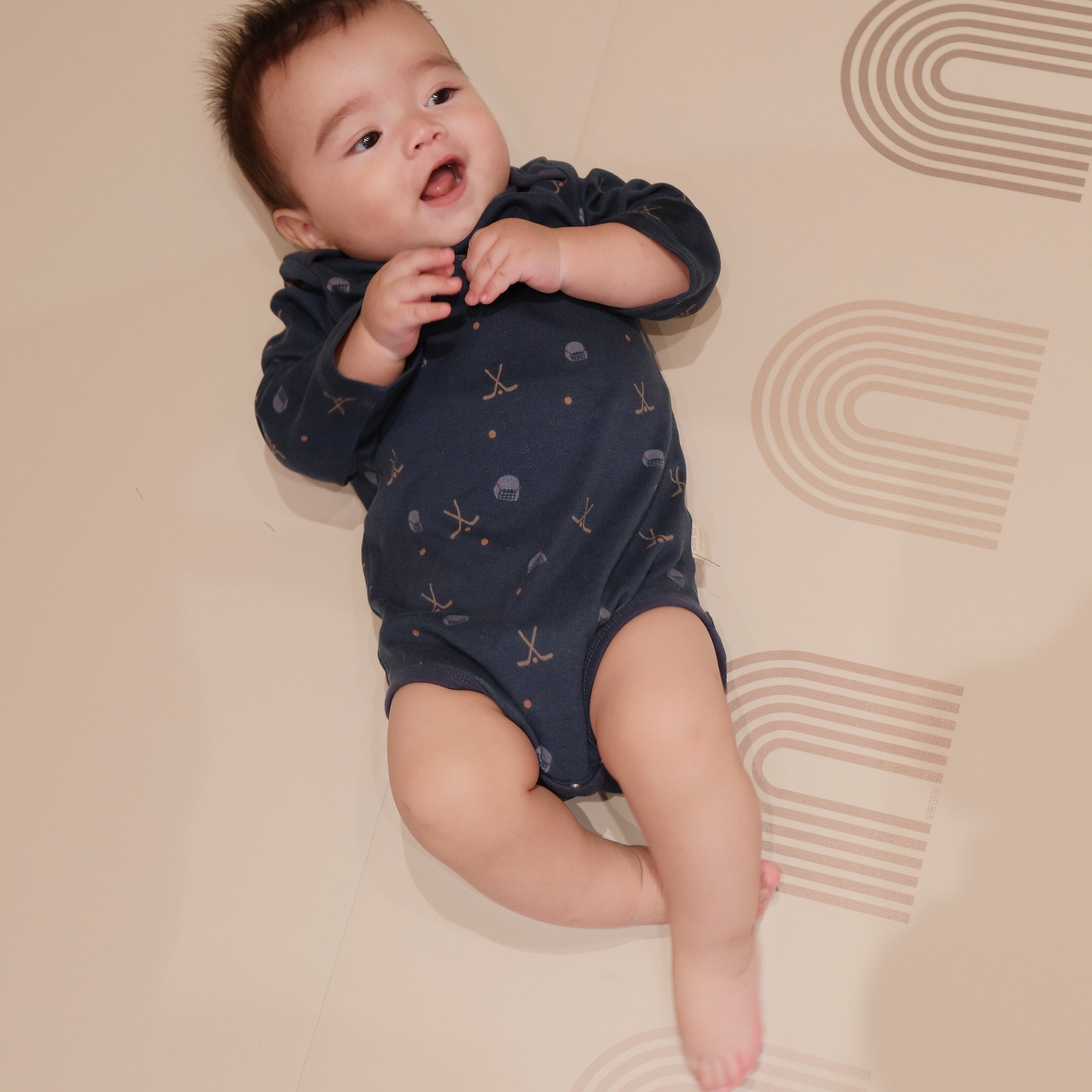 Baby in a navy blue onesie with hockey pattern lying on a beige surface