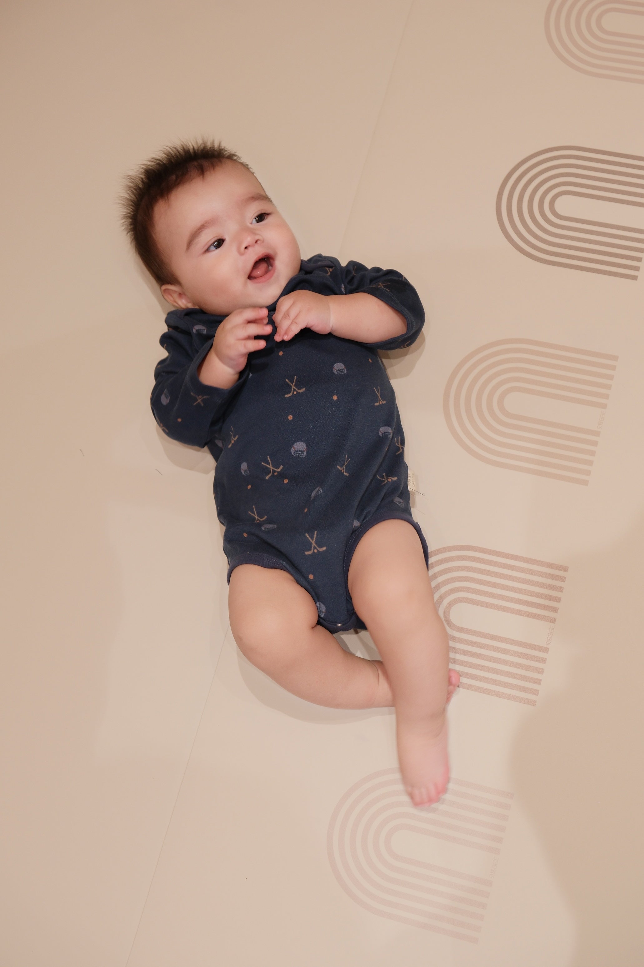 Baby in a navy blue onesie with hockey pattern lying on a beige surface