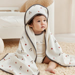 Baby wrapped in a white blanket with penguin patterns on a beige carpet.