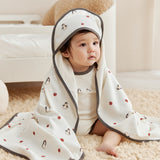 Baby wrapped in a white blanket with penguin patterns on a beige carpet.