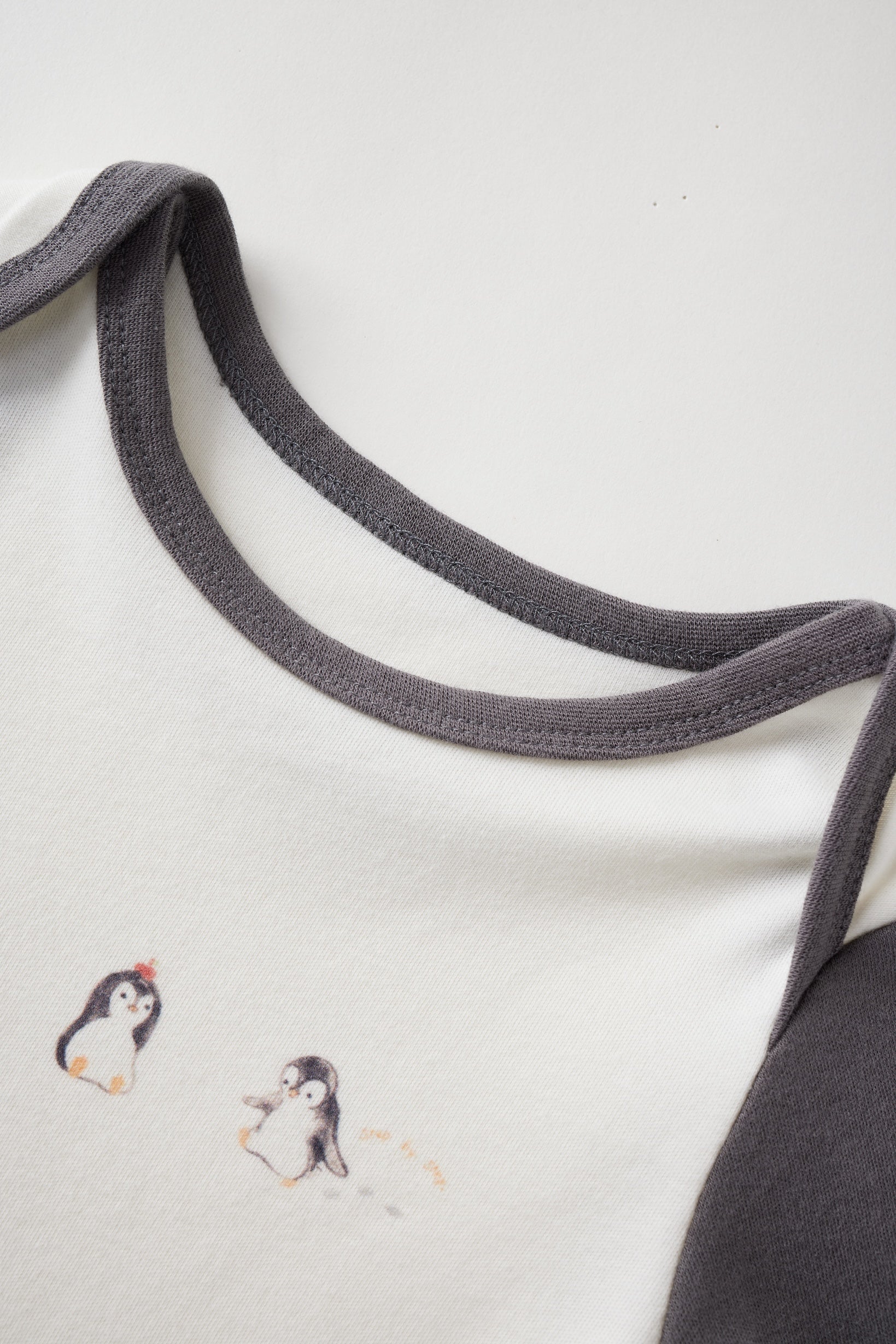 Close-up of a baby outfit with embroidered penguins and gray trim on a white background
