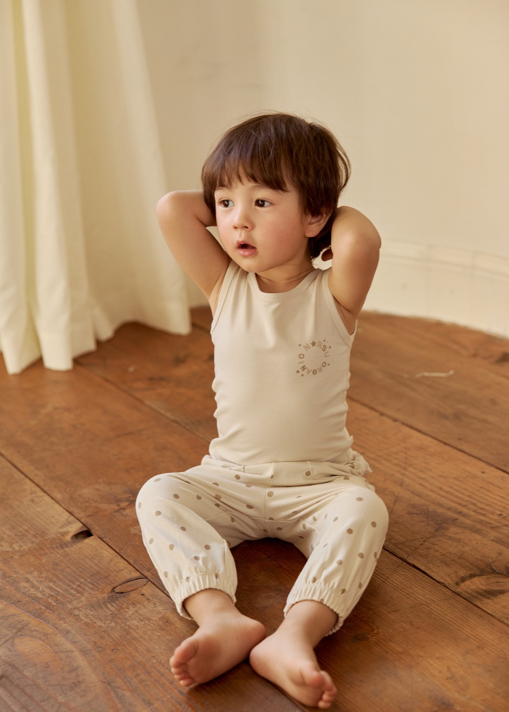 A little boy in an organic bamboo tank top sits on the floor