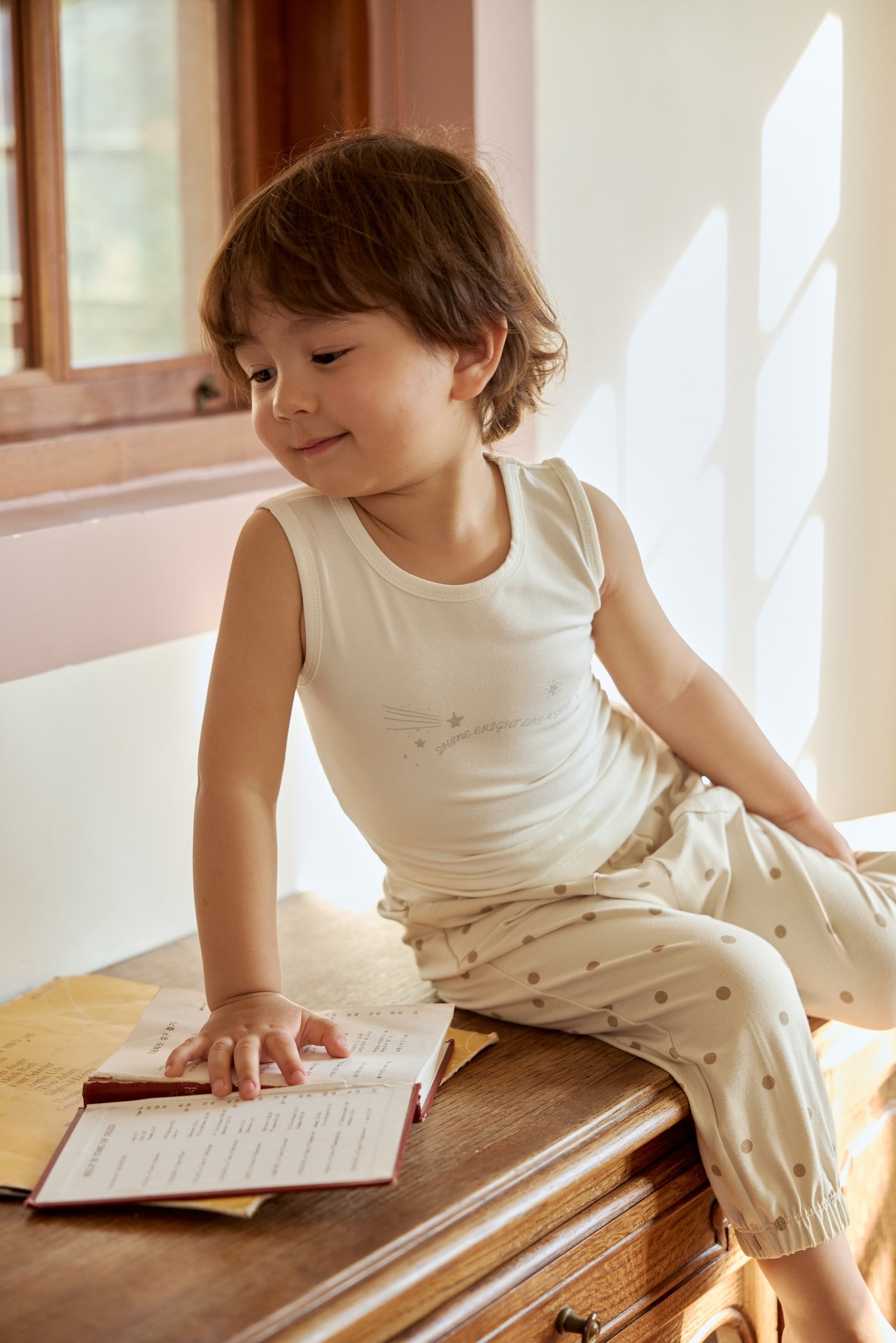 A little boy in an organic bamboo tank top sits on the table deeply engrossed in his book.
