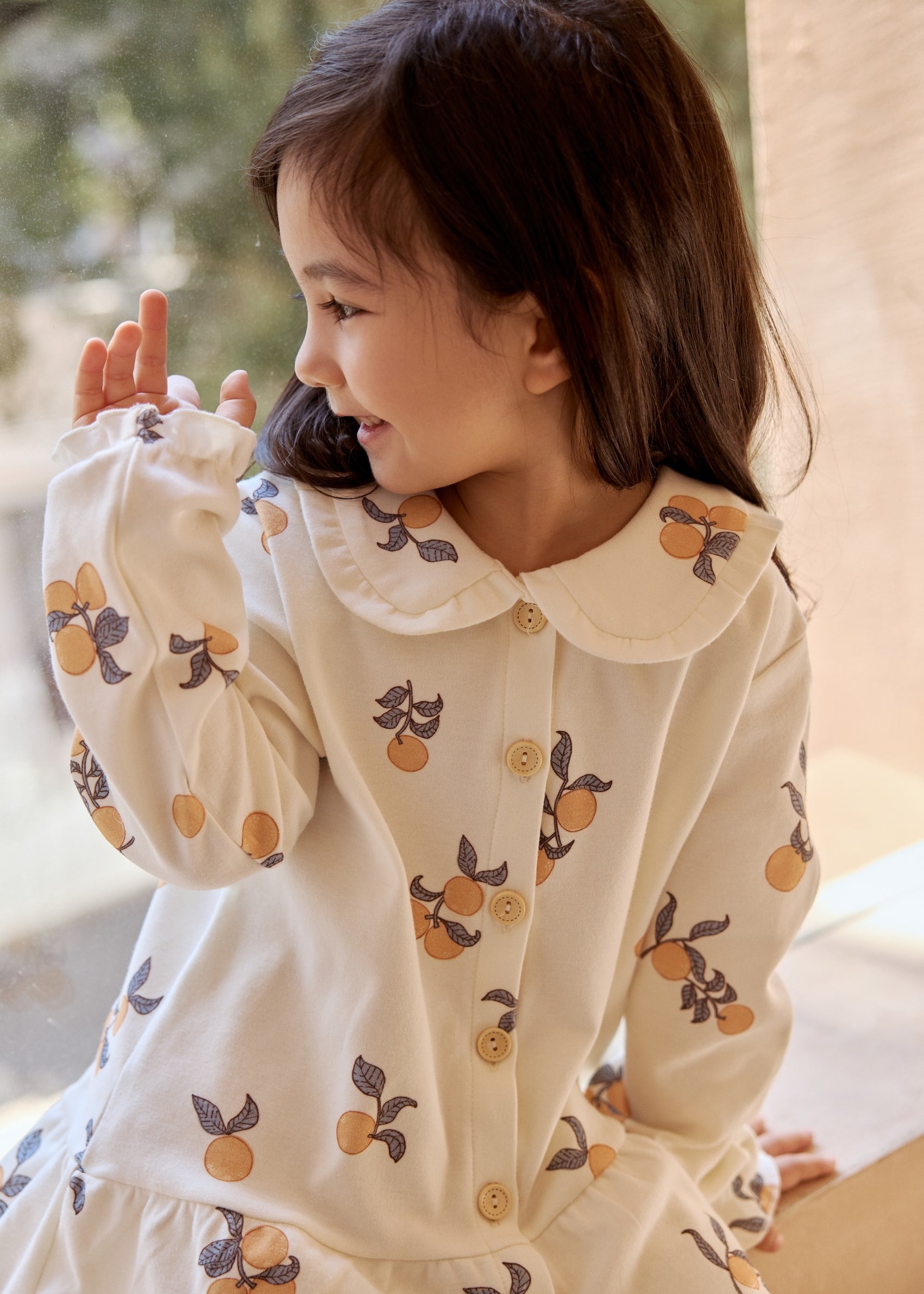  A cheerful girl wearing a white shirt with orange print and a ruffle collar, radiating joy and style