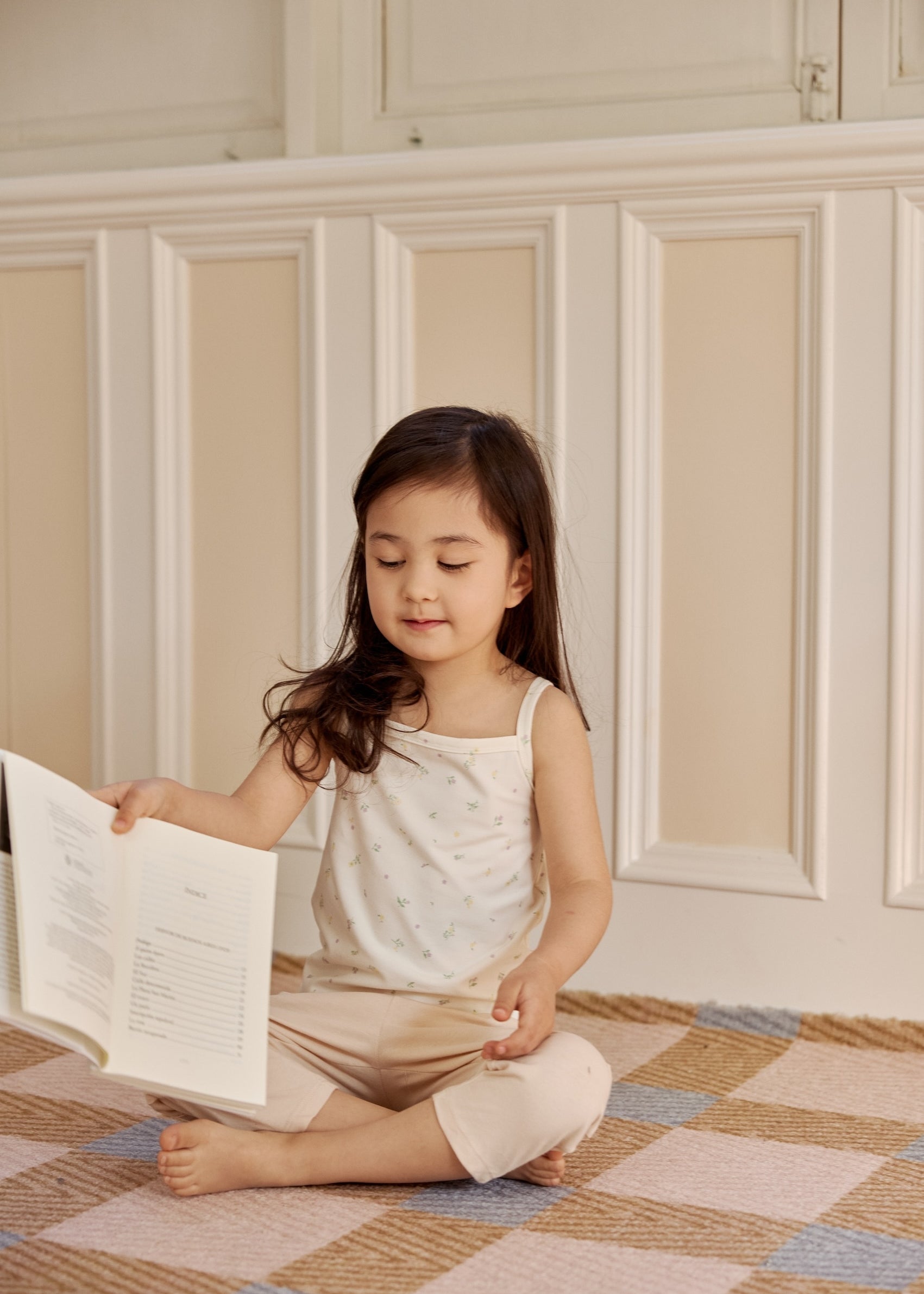 A little girl in an organic bamboo tank top sits on the floor, deeply engrossed in her book