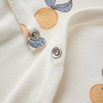 Close-up of a white garment with orange and blue leaf patterns and metal buttons.