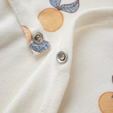Close-up of a white garment with orange and blue leaf patterns and metal buttons.