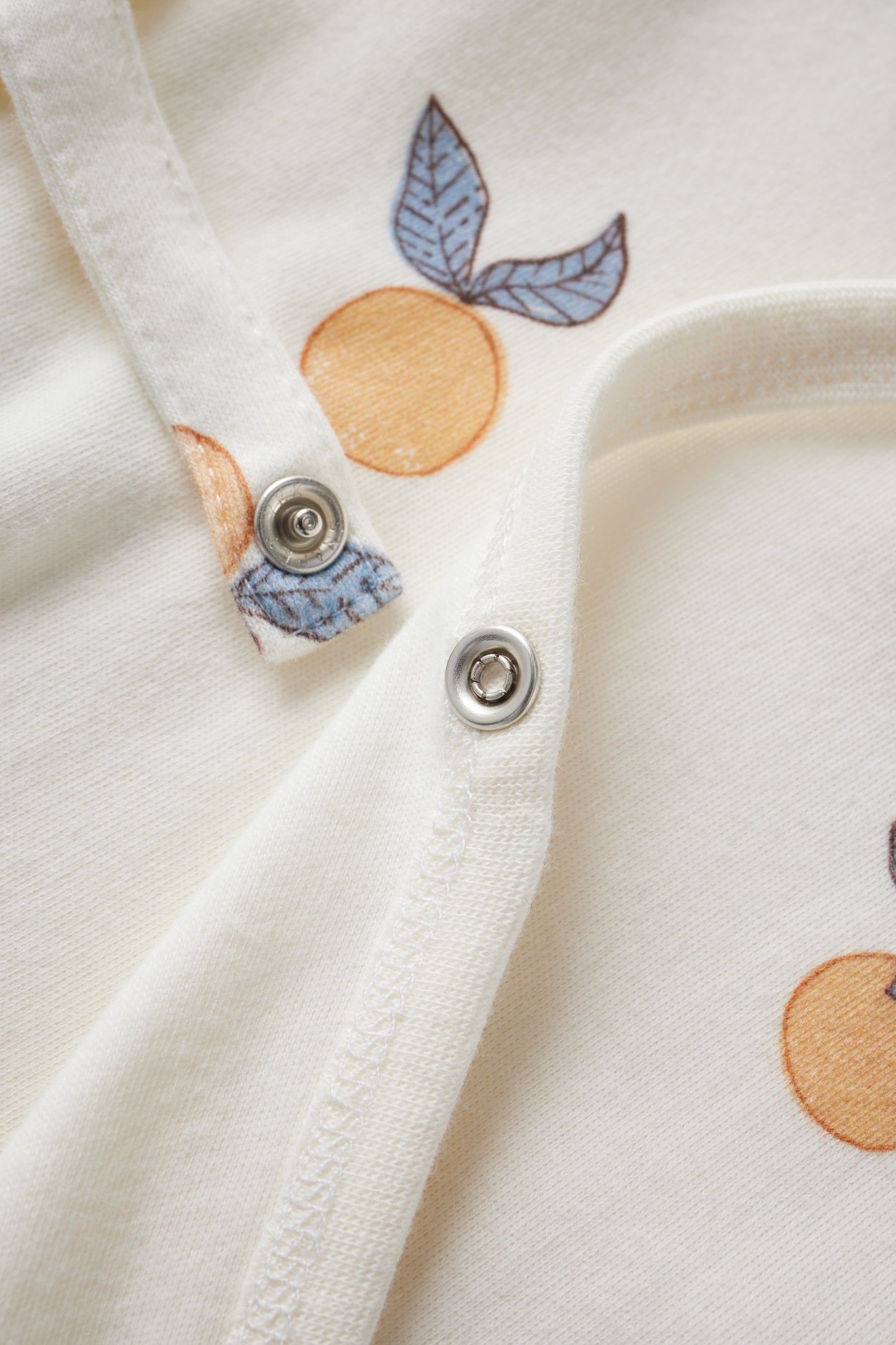 Close-up of a white garment with orange and blue leaf patterns and metal buttons.