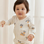 Child wearing a cream-colored outfit with fruit pattern in a softly lit room.