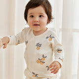 Child wearing a cream-colored outfit with fruit pattern in a softly lit room.