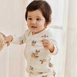 Baby wearing a white outfit with fruit patterns in a softly lit room.