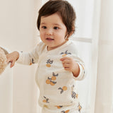 Baby wearing a white outfit with fruit patterns in a softly lit room.