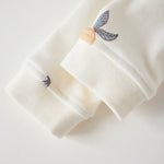 Close-up of a white garment with embroidered butterfly details on a light gray background
