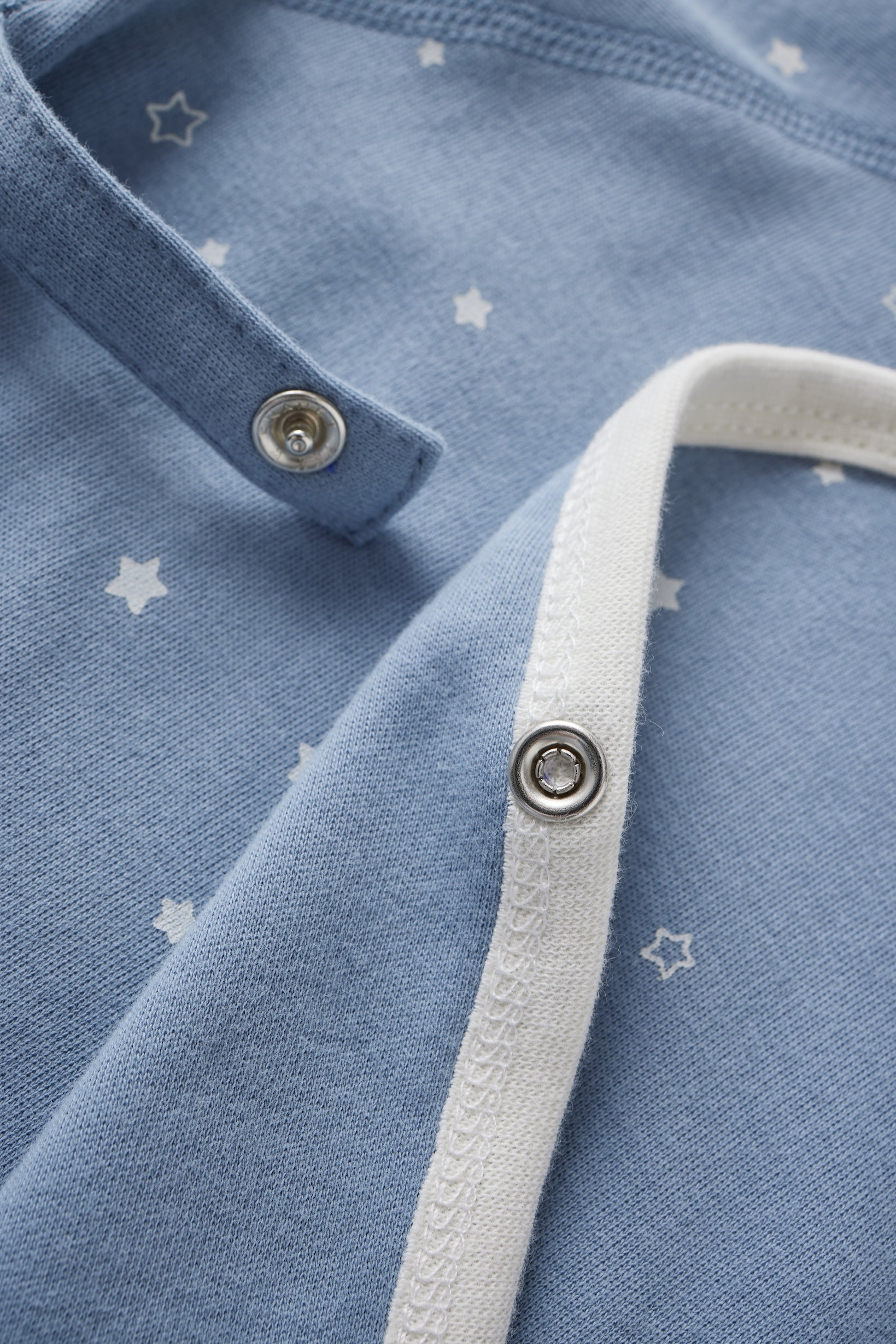 Close-up of a blue baby shirt with white star patterns and white trim.