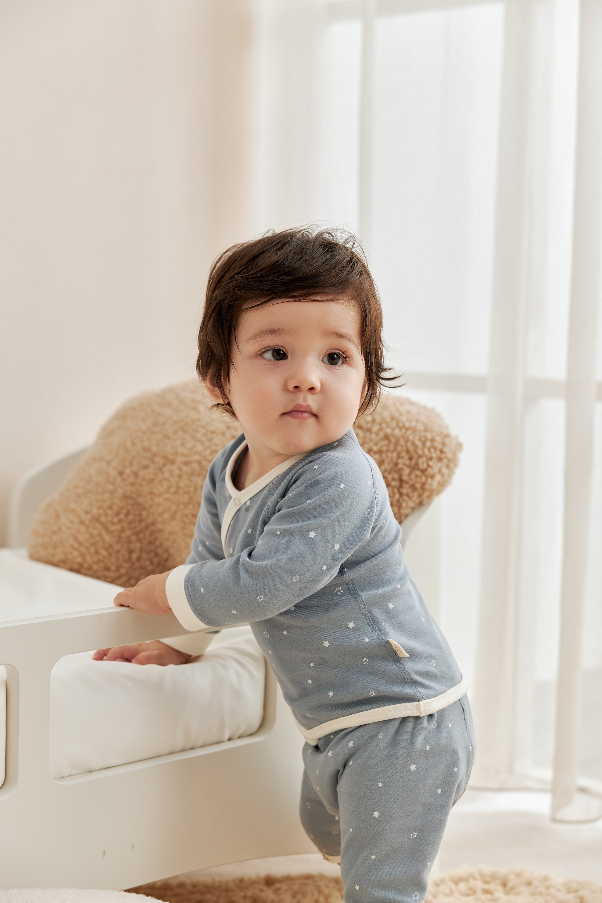 Child wearing a light blue outfit with white starry  in a bright room.