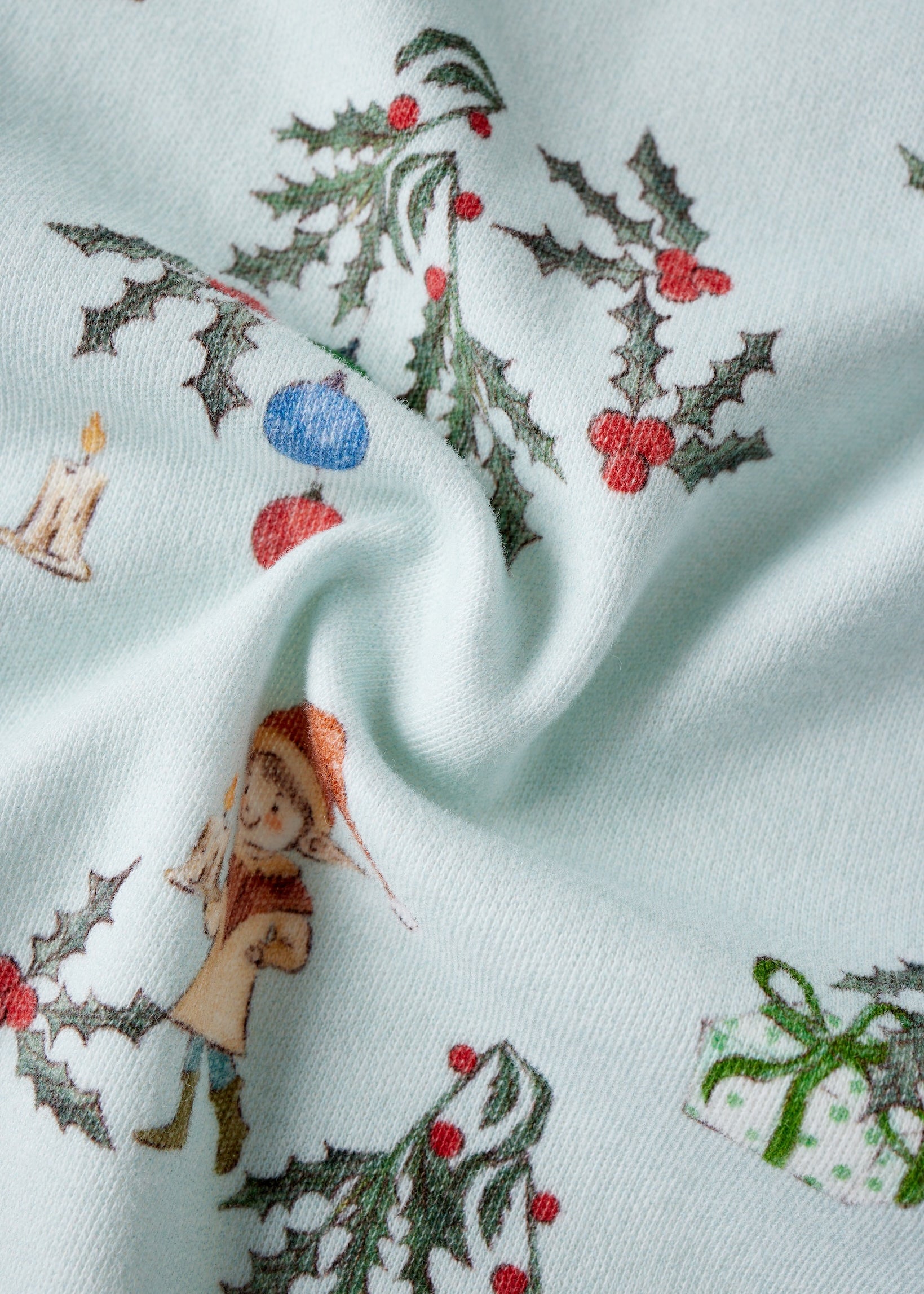 Fabric with Christmas-themed design featuring holly, berries, and a small figure on a light blue background.