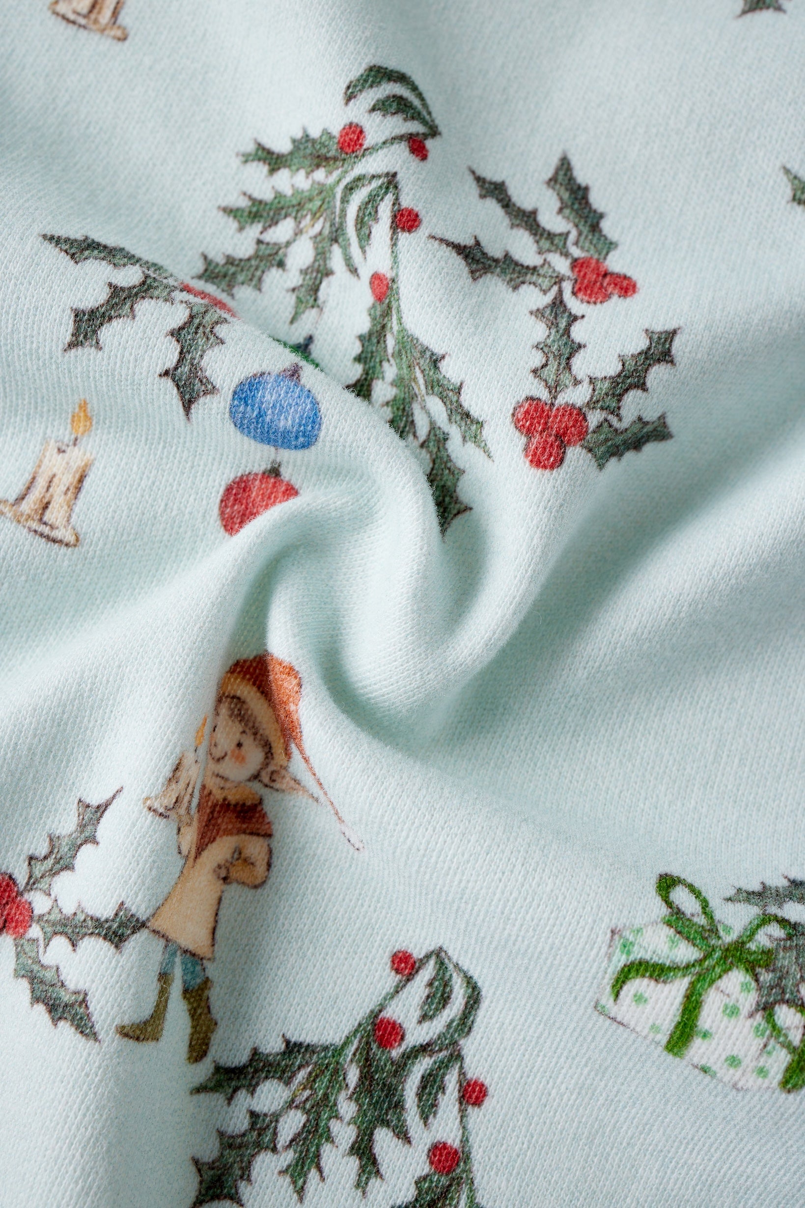 Fabric with Christmas-themed design featuring holly, berries, and a small figure on a light blue background.