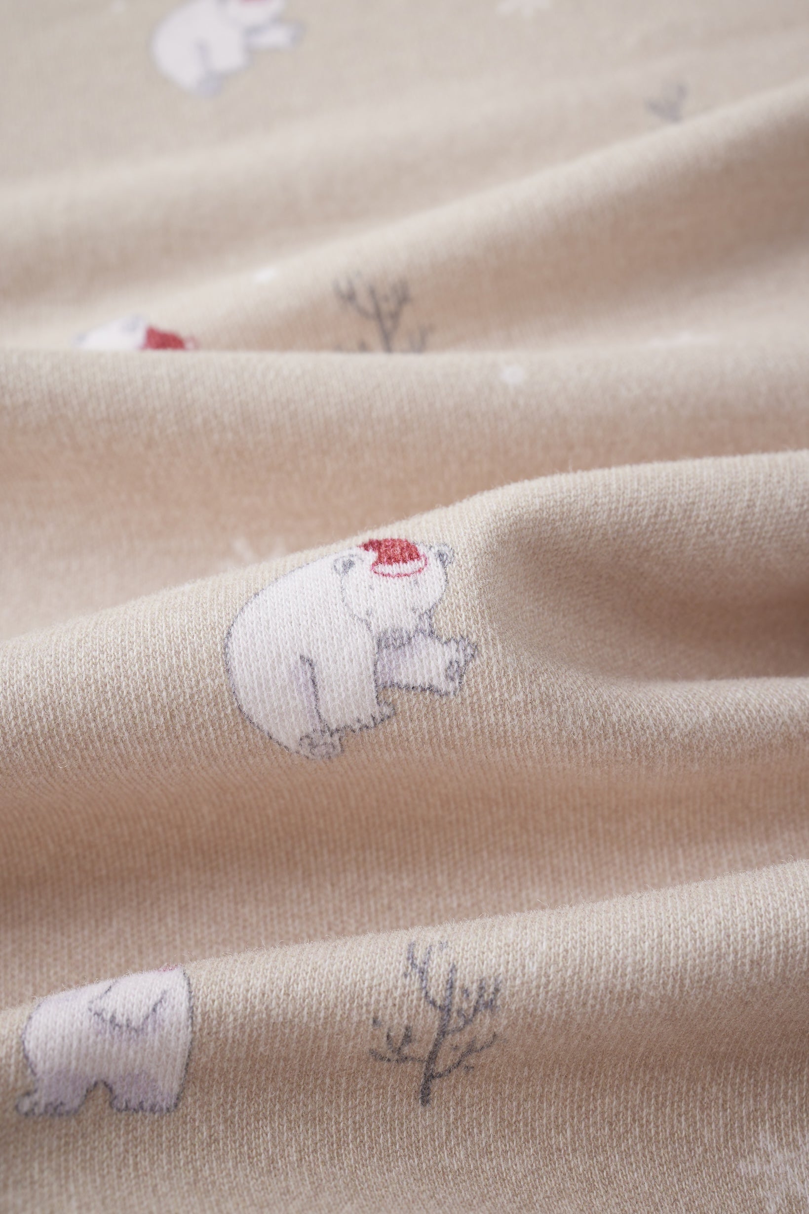 Close-up of beige fabric with embroidered polar bears and plants.