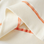 Close-up of a white garment with orange stitching on a light background